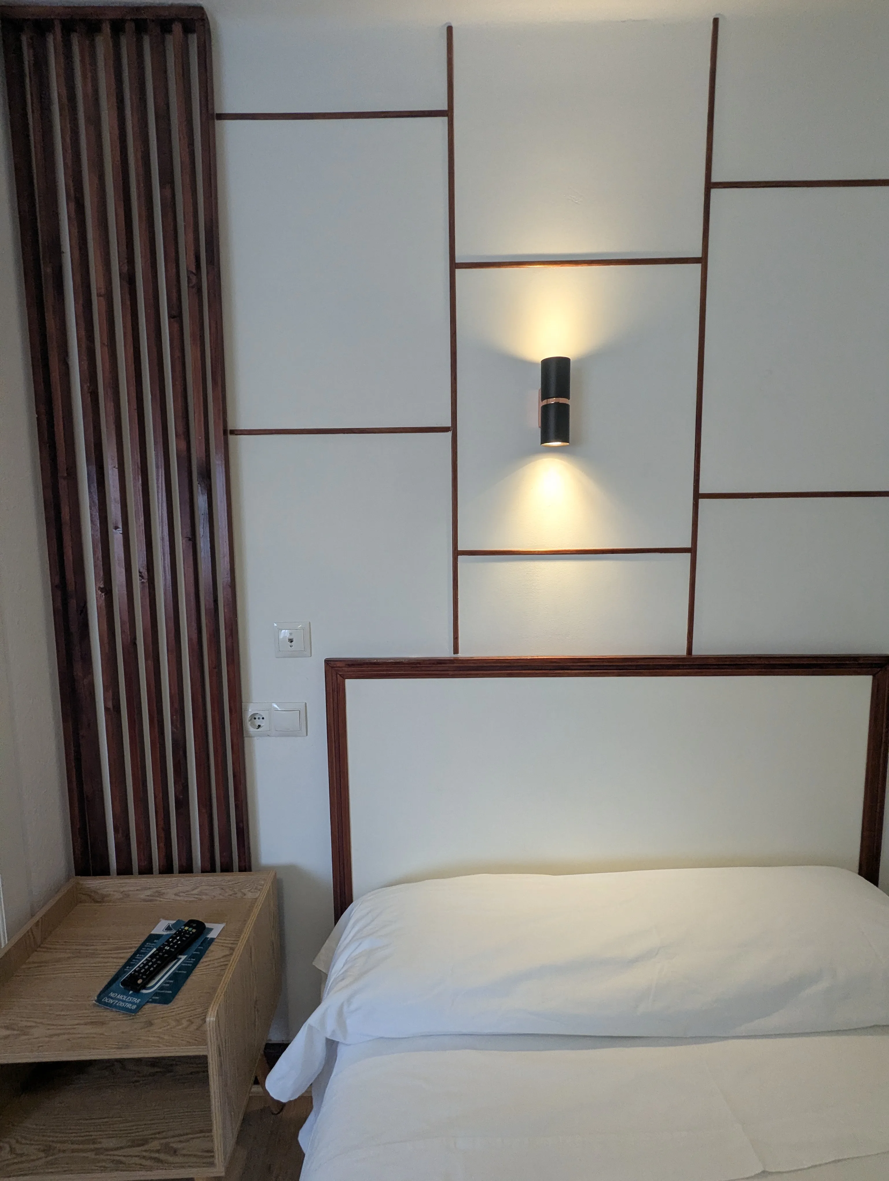 Habitación individual de Hostal La Mexicana con aplique cilíndrico encendido sobre panelado geométrico y separador de bambú